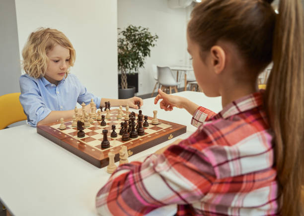 istock Change with each move. Concentrated little caucasian boy planning his move while playing chess with friend, sitting together at the table in school 1354688211