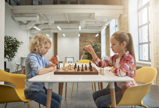 istock Two smart little children, boy and girl developing chess strategy, playing board game, sitting together at the table in school 1354688220