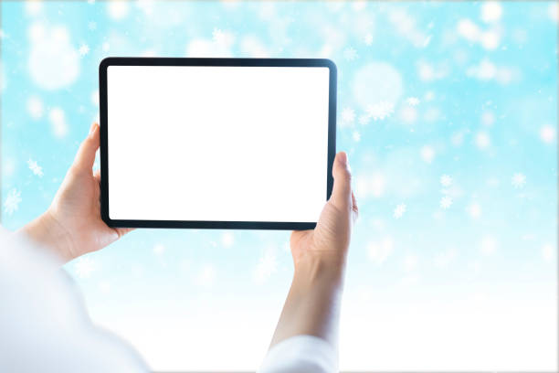 lady hand holding tablet with blank white screen on blury christmas background with snow and light bokehs
