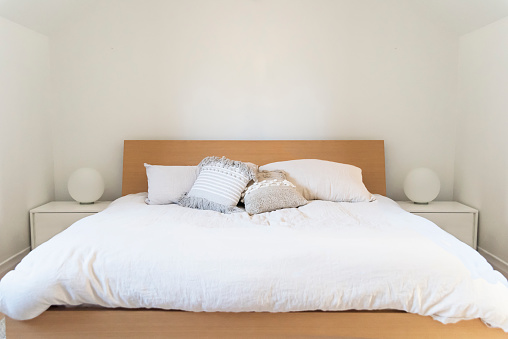 Minimalist bedroom environment. Pillows, cushions and bedsheet on white background. Lamps and night tables. Horizontal indoors shot with copy space. No people.