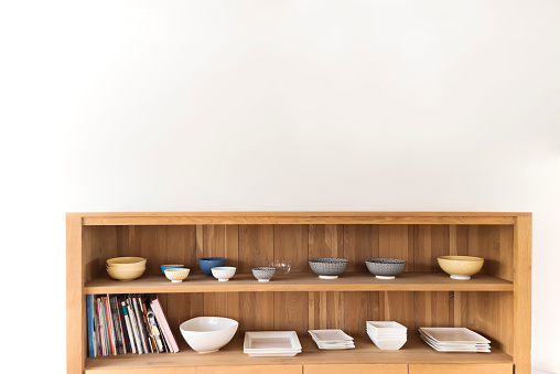 Minimalist kitchen environment. Open cabinet with bowls and recipes books on white background.  Horizontal indoors shot with copy space. No people.