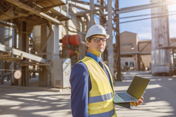 istock Male worker with laptop standing outdoors at factory 1354697121