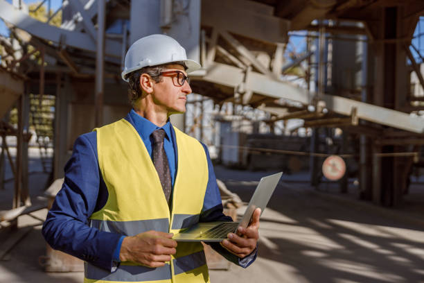 istock Male worker with laptop standing outdoors at factory 1354697122