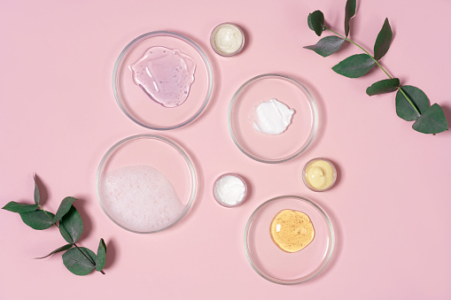Cosmetic products, scrub, face serum and gel in many petri dishes on a pink background. Cosmetics laboratory research concept