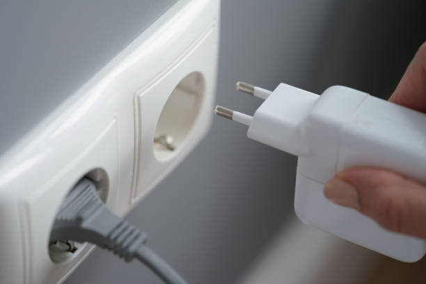 istock Hand inserts laptop power supply into the socket 1354699960