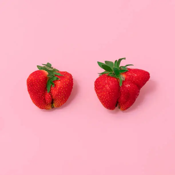Top view of deformed strawberries on soft pink background. Ugly food movement concept
