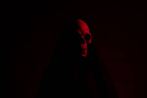 Skeleton in red lighting holding large orange pumpkin on dark background for Halloween decor.