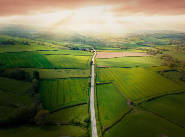 vista aerea che guarda giù su una strada rurale nella campagna del regno unito con un'auto che corre lungo di essa. - english village immagine foto e immagini stock