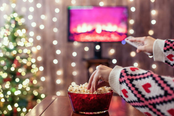istock Christmas eve. Alone woman eating popcorn, watching tv, switching channels using remote control. Home cinema. Cropped, close up 1354710965