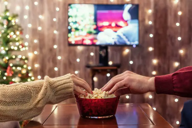 Photo of Christmas eve. Couple watching tv and eating popcorn. Home cinema. Cropped, close up