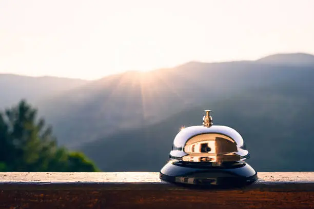 Photo of Silver vintage bell on village reception desk in the morning sunrise mountain . Eco, camping hotel service, registration.