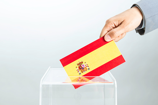 Hand of business person  is inserting Spanish flag into ballot box. Representing voting in Spain.