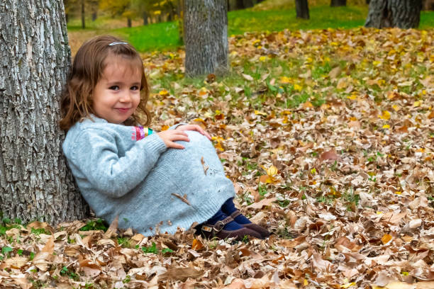 istock Little girl sitting on the ground leaning on a tree trunk 1354720119
