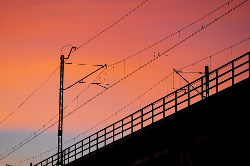 Sunset sky with silhouette of railway bridge electric traction and balustrade.