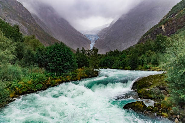 Scenic view on Briksdal glacier, river and Norwegian mountains against cloudy dramatic sky in Norway