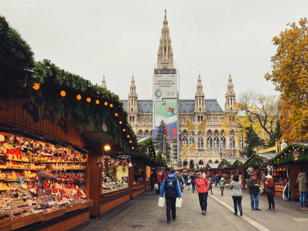 Vienna, Austria - November 20, 2019: Austrian Christmas huts, vendor retailing colorful baubles and craft toys. Bazaar sale in evening time. Magical celebration atmosphere. People shopping traditional gifts.
