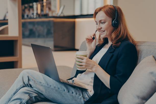 istock Young dispatcher lady working remotely via wireless headset and laptop, sitting on sofa in teahouse 1354731433