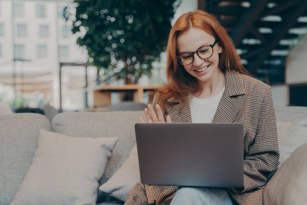 istock Happy red-haired business woman waving at laptop webcam during web conference with client 1354731470