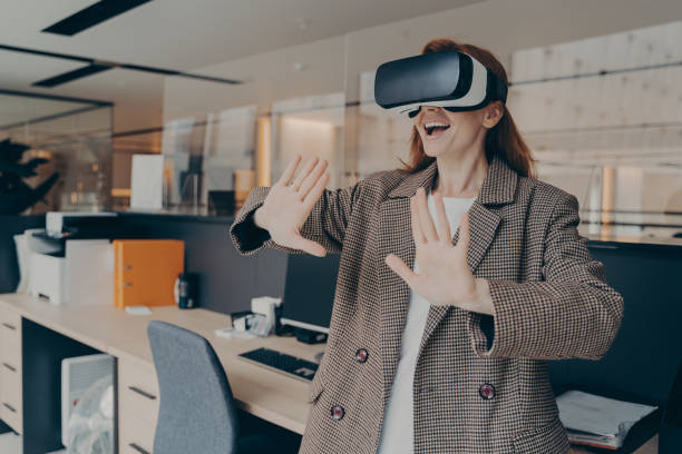 istock Woman wearing VR headset having fun in virtual reality game while standing in office 1354731471