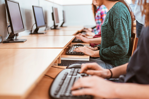 Students attending an exam in university computer lab with a professor supervising them and their hands in focus.