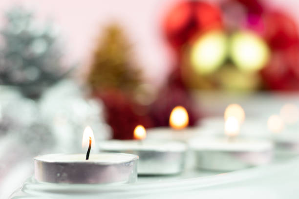 White Tealight Candles Illuminated In Row With Colorful Blur Bokeh Decorations On Light Pink Background. Theme For Merry Christmas And Happy New Year