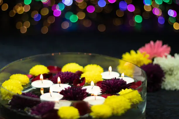 Floating Tealight Candles Illuminated In Decorative Urli Crystal Bowl Filled With Water And Flowers. Colorful Bokeh On Dark Background. Theme For Shubh Deepawali, Merry Christmas And Happy New Year