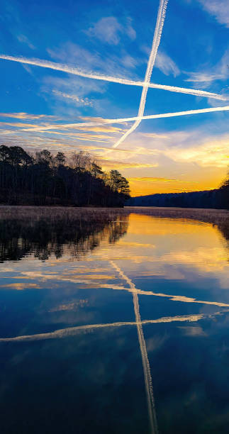 Contrails crossing in the sky above early morning sunrise reflected stock photo