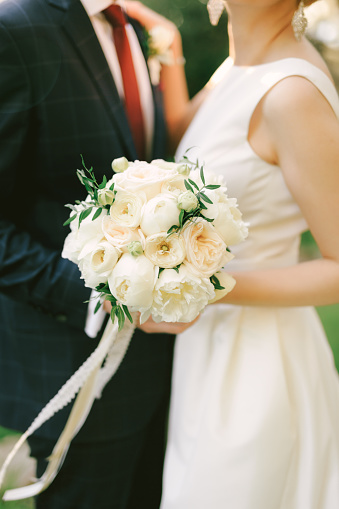 Groom in a blue checkered suit hugs bride in a white dress with a bouquet of flowers. Close-up. High quality photo