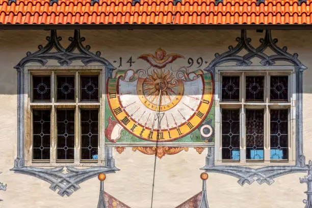 A sundial on a house wall between two windows, framed by illusion painting