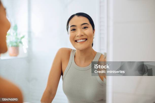 Morning Routine Portrait Of A Beautiful Asian Woman Looking At Herself In The Mirror Holding A Beauty Care Product Stock Photo - Download Image Now