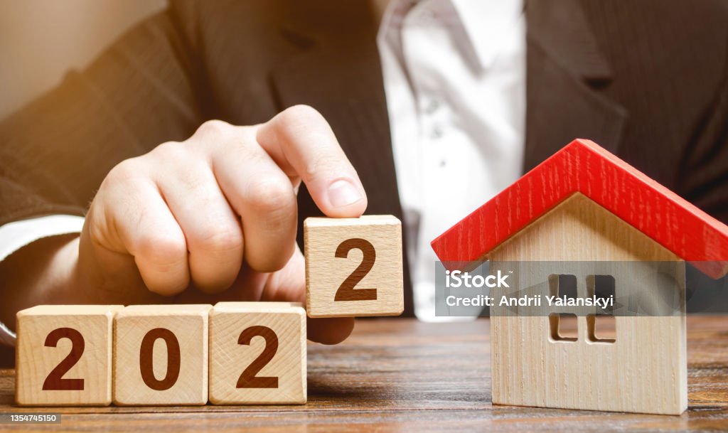 A businessman making 2022 out of blocks near house. Concept of the real estate market in the new year. Forecast of prices and offers, new trends and tendencies. Investment plans. Mortgage loan. Real Estate Stock Photo
