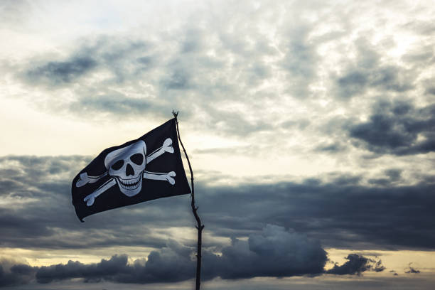 Jolly roger pirate's flag against dramatic sunset sky with clouds and copy space in vintage blue colors