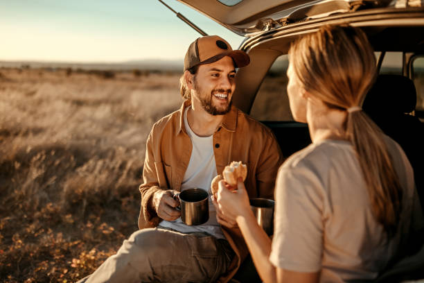 Happy couple having breakfast in car trunk on field