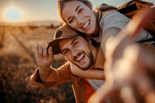 Portrait of cheerful couple having fun while piggybacking on field during sunset