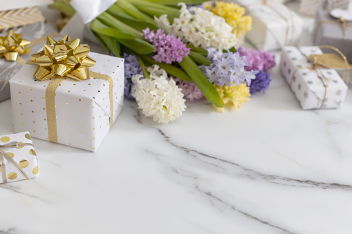 trendy composition with festive wrapped gift boxes ribbon bow decorated by bloom flowers. Stylish packing presents with natural blossom on white marble. Beautiful holiday celebrating