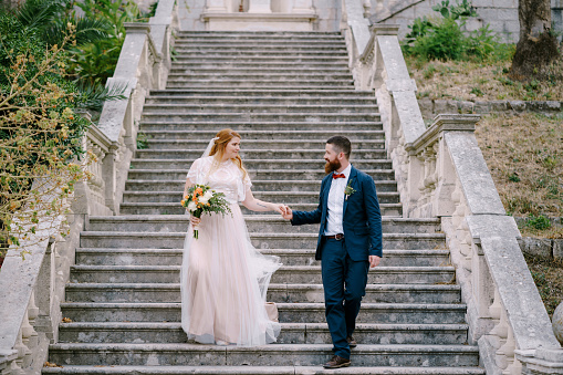 Bride and groom descend the steps holding hands. High quality photo