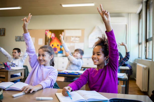istock Schoolchildren at classroom with raised hands answering teacher's question and smiling. 1354759404