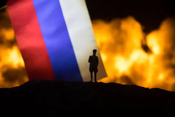 Russia flag on burning dark background. Concept of crisis of war and political conflicts between nations. Silhouette of armed soldier against a Russian tricolor. Selective focus