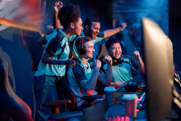 Team of professional cybersport gamers celebrating success in gaming club Multiracial cybersport gamers expressing success while raising hands up and smiling during participation in esports tournament in computer club headset photos stock pictures, royalty-free photos & images