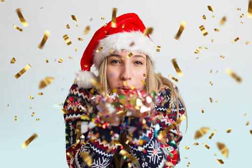 A beautiful woman with a Santa hat blowing confetti