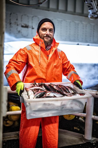 Pescador con caja de pescado fresco en la cubierta del barco de pesca photo