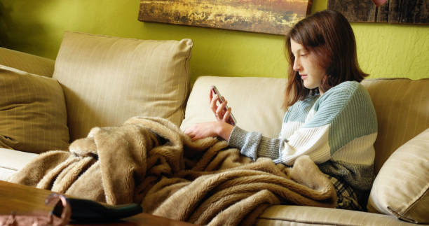 10代の女性は、彼女の携帯電話でメディアを見ながら集中 - homewares cushion fake fur blanket ストックフォトと画像