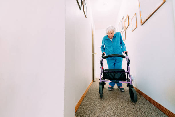 Wide Angle Shot of an Independent Elderly Woman Walking Through Her Home with a Mobility Walker Wide Angle Shot of an Independent Elderly Woman Walking Through Her Home with a Mobility Walker on Carpet, which can be a Tripping Hazard for many Senior Citizens. She uses a Mobility Walker to Avoid a Fall. slow walk stock pictures, royalty-free photos & images