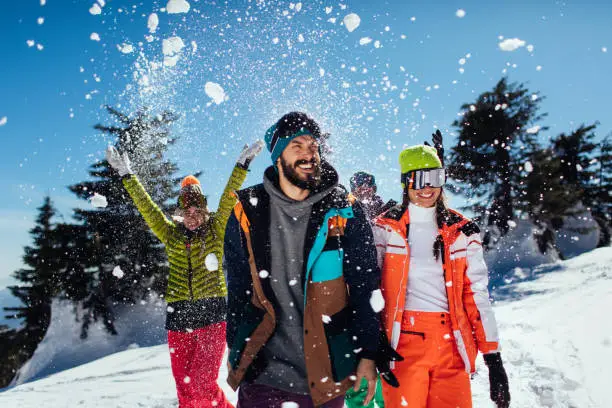 Group of four friends throwing snow in the air while enjoying their mountain trip