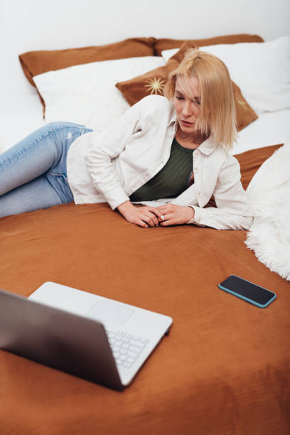 istock Young woman lying on her bed looking at her laptop screen 1354770554