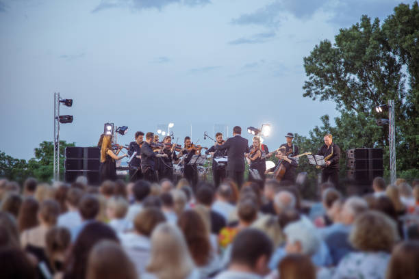 istock Orchestra performing live concert for audience under blue sky 1354772462