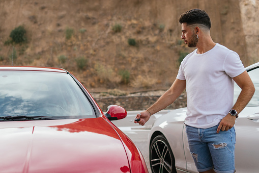 Scene of a handsome man opening and activating his automobile with his car keys because is about to leave a viewpoint.