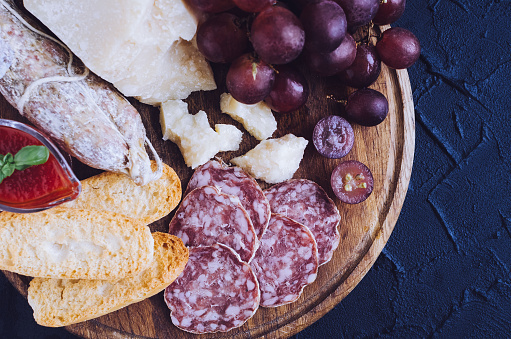 Board with mediterranean appetizers, tapas or antipasti. Assorted Italian style banquet food set. Delicious snack on party. Chopping board with salami, bread, sauce, grapes and Parmesan cheese. Top view.