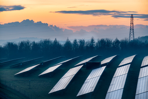 Multiple solar panels reflecting the fading winter sunlight at dusk, and glowing afterlight in the sky beyond,in the rural countryside of southern Britain.