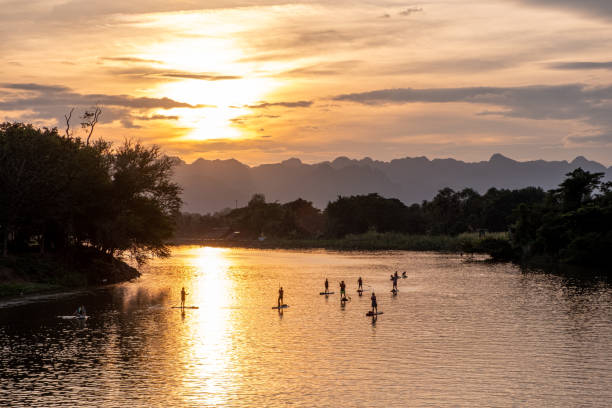 paddleboarders au coucher du soleil sur une rivière de la jungle - kanchanaburi province travel asia forest photos et images de collection